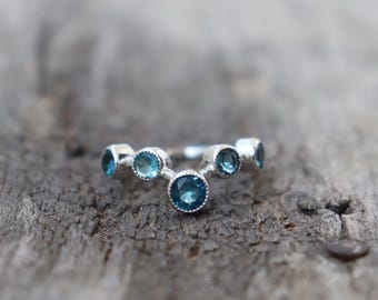 May include: A silver ring with a row of blue gemstones set in a curved shape.