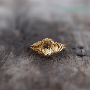 Peut inclure: Une bague en or avec un motif délicat de feuilles et une pierre ovale brun clair.