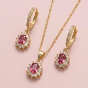 May include: A gold jewellery set consisting of a necklace and two hoop earrings. Each piece features an oval-cut pink gemstone surrounded by a halo of small white stones. The hoop earrings have pavé-set white stones along the front of the band.