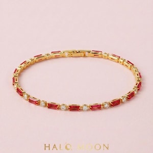 May include: A gold-toned bracelet featuring alternating baguette-cut red stones and round clear stones in a continuous link design. The piece includes a secure clasp mechanism and is positioned above the gold text HALO MOON.