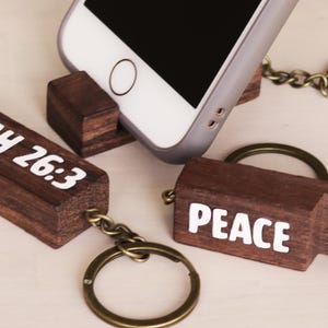 May include: Two wooden phone stand keychains with a metal ring. One keychain has the text "ISAIAH 26:3" and the other has the text "PEACE".