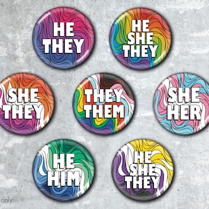 May include: Set of 7 colorful round buttons with rainbow swirl designs. Each button features a different pronoun combination, including "He Him", "She Her", "He They", "She They", "They Them", and "He She They".