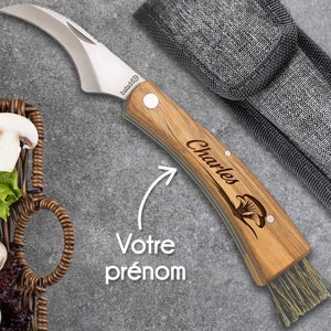 Peut inclure: Un couteau à champignons avec une lame incurvée en acier inoxydable et un manche en bois gravé du nom "Charles" et d'une illustration de champignon. Le couteau comprend une brosse et est livré avec un étui en tissu gris. Le texte "Votre prénom" est également visible.