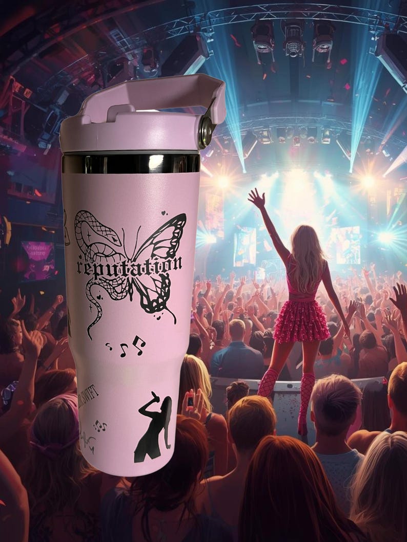 May include: A light pink tumbler with a black butterfly and the word "reputation" printed on it. The tumbler also features musical notes and a silhouette of a singer. The background shows a concert stage.
