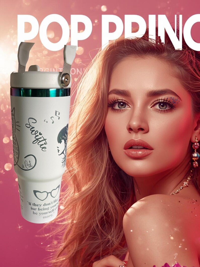 May include: White tumbler with a handle and a lid. The tumbler has a green band and a design that includes a cat, musical notes, and the word "Swiftie". The tumbler also has the quote "If they don't like you for being yourself, be yourself more."