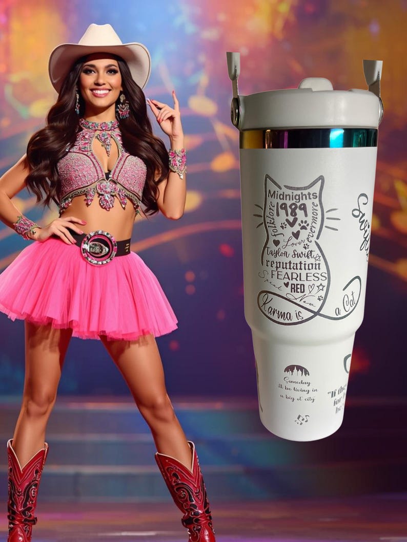 May include: A white travel mug with a cat silhouette design and the text "Midnights 1989 Taylor Swift's reputation FEARLESS RED Karma is a Cat". The mug has a silver rim and handle attachments.