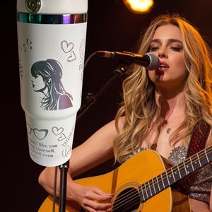 May include: White insulated tumbler with a handle, featuring a silhouette of a woman, musical notes, hearts, and the text "don't like you, love yourself, even more." The tumbler has a silver rim and a holographic band.