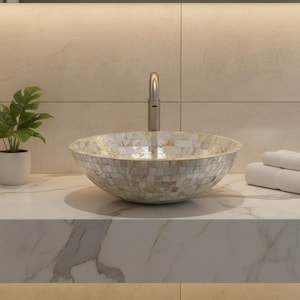 Puede incluir: Un lavabo con mosaicos y un grifo plateado se encuentra sobre una encimera de mármol. Una pequeña planta en maceta y dos toallas blancas dobladas también están sobre la encimera. El lavabo es el punto focal de un baño moderno.