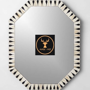 May include: Octagonal mirror with a white bone inlay frame and black teardrop accents. The frame is surrounded by a silver mirror. The mirror has a black and gold logo that says "Auric Art".