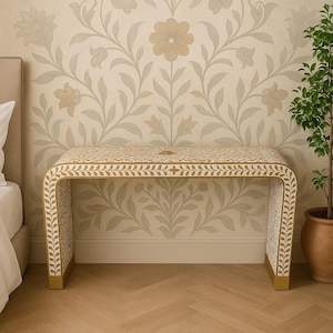 Könnte beinhalten: Ein weiß-goldener dekorativer Schreibtisch mit geschwungenem Design. Der Schreibtisch hat ein Blumenmuster auf der Oberseite und den Seiten mit goldenen Akzenten an den Beinen. Der Schreibtisch steht vor einer floralen Tapete.