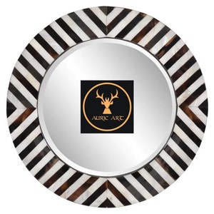 May include: Round mirror with a black and white chevron patterned frame made of bone. The mirror has a silver backing and the frame is made of bone. The mirror has a logo in the center that says "Auric Art".