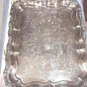 Puede incluir: Una taza de cerámica blanca con un asa negra y el texto "But First, Coffee" en negrita negra. La taza se encuentra sobre un fondo borroso, sugiriendo un ambiente acogedor.