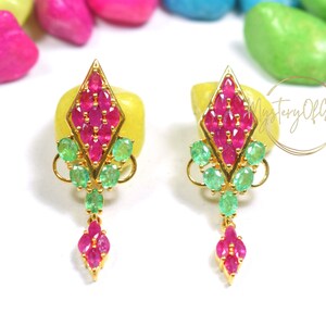 May include: A pair of gold earrings with a diamond-shaped design. The earrings are adorned with pink and green gemstones.