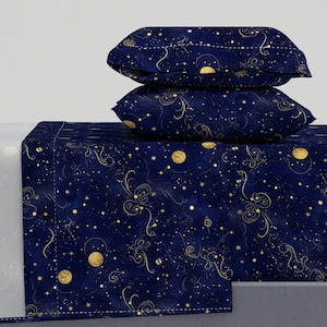 Puede incluir: Un juego de sábanas azul marino con un diseño celestial. El juego incluye una sábana bajera, una sábana encimera y dos fundas de almohada. El patrón presenta estrellas doradas, lunas y líneas onduladas. Las sábanas están hechas de un material suave y cómodo.