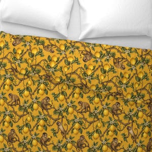 Puede incluir: Una funda nórdica con un patrón repetitivo de monos posados en ramas de limonero con limones amarillos, hojas verdes y flores blancas sobre un fondo amarillo mostaza, mostrada con dos almohadas blancas en la parte superior.