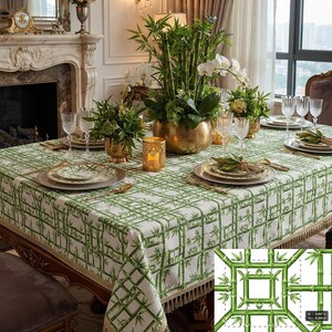 May include: A rectangular tablecloth featuring a green bamboo lattice pattern on a white background with decorative fringe trim along the edges. The fabric displays a repeating grid design of bamboo stalks and leaves, covering a large dining table.