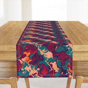 May include: A rectangular table runner with a vibrant abstract design. The pattern features swirling shapes in shades of burgundy, teal, and peach. The runner is placed on a wooden table, adding a pop of colour to the setting.
