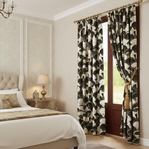 Puede incluir: Interior de dormitorio con cama con ropa de cama crema y cojines decorativos. Las cortinas estampadas en negro, blanco y dorado enmarcan la ventana. Una borla dorada sujeta la cortina. Ambiente elegante.