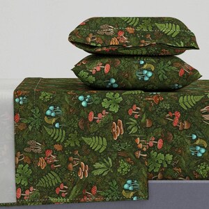 Puede incluir: Juego de cama con estampado de bosque, que incluye una sábana bajera y dos fundas de almohada. El tejido verde oscuro presenta ilustraciones de setas, helechos y otros elementos del bosque en tonos rojos, marrones y azules.