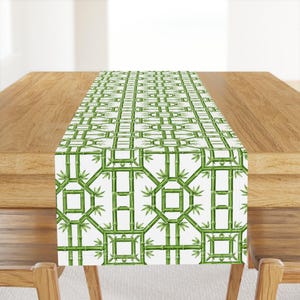 May include: A rectangular table runner featuring a repeating geometric pattern of green bamboo stalks on a white background. The design consists of interconnected bamboo segments forming square and octagonal shapes with small green leaves.