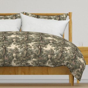May include: A duvet cover and two matching pillow shams featuring a repeating toile pattern in shades of dark green and cream. The design depicts a landscape with large trees, stone urns filled with flowers, and distant architectural structures.