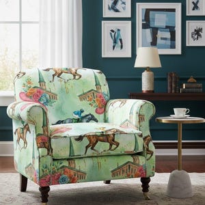 Puede incluir: Sillón tapizado con fondo verde claro y temática de carreras de caballos. La silla presenta imágenes de caballos, jinetes y edificios. La silla tiene patas de madera oscura y brazos enrollados.