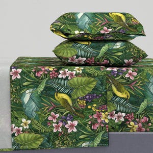 May include: Bedding set featuring a vibrant jungle-themed pattern. The design includes yellow birds, pink flowers, and lush green foliage. Two pillows are stacked on top of a bedspread, all with the same print.