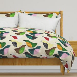 Puede incluir: Una cama con una funda nórdica y fundas de almohada color crema. La funda nórdica presenta un patrón repetido de pájaros coloridos en tonos verdes, marrones, amarillos, rosas y rojos. La estructura de la cama es de madera clara.