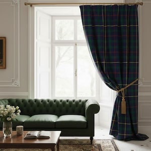 Op de afbeelding: Een woonkamer met een donkergroene bank, een houten salontafel en een raam met geruite gordijnen. De gordijnen zijn voornamelijk donkerblauw en groen met gele en rode accenten. Een gouden gordijnroede en kwast maken het geheel af.