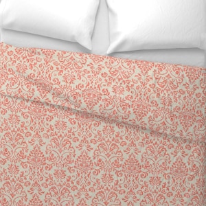 May include: A coral and cream-colored damask pattern bedspread with two white pillows. The floral design is repeated across the fabric. The bedspread is folded over the bed.