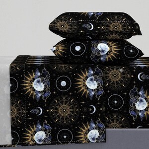 Puede incluir: Juego de cama negro con temática celestial con un patrón repetido de soles, lunas, estrellas y diseños de brújulas en oro y blanco. El juego incluye dos fundas de almohada y una sábana bajera. El diseño está sobre un fondo negro.