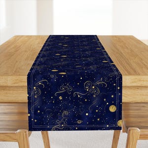 May include: A navy blue table runner with a celestial design. It features gold stars, planets, and swirling patterns against a dark blue background. The edges are bordered with a thin white line, creating a decorative accent.