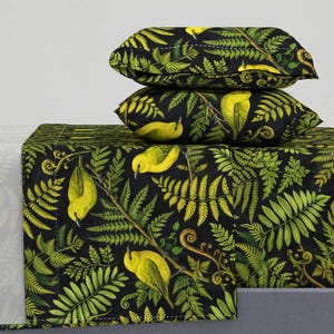Puede incluir: Dos cojines decorativos y un camino de cama con fondo negro, adornados con un estampado de helechos verdes y pájaros amarillos. Los cojines están apilados sobre el camino de cama, creando un diseño coordinado. El tema es la naturaleza y botánico.