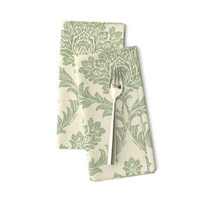 May include: A folded fabric napkin featuring a light green damask pattern on an off-white background, with a silver-toned metal fork placed vertically on top of the fabric. The napkin has a rectangular shape with visible stitched edges.
