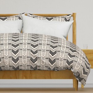 Puede incluir: Una cama con estructura de madera y funda nórdica y fundas de almohada color crema. La funda nórdica y las fundas de almohada presentan un patrón geométrico negro de líneas verticales y formas de flecha.