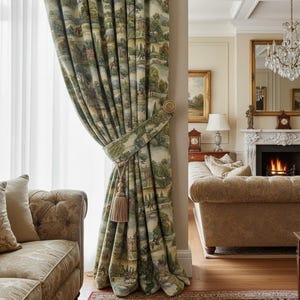 May include: A pair of patterned curtains with a landscape design, tied back with a matching fabric tieback and a tassel. The curtains are a mix of green, beige, and blue, and are hanging in a room with a sofa and a fireplace.