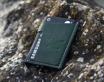 May include: A green leather wallet with a stitched edge and a small eagle logo that says "Magor Leathercraft". The wallet is holding a black Samsung Pay card.