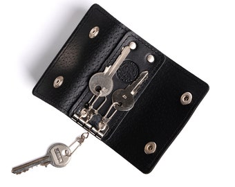 May include: Black leather key holder with a metal key ring and three keys. The key holder has a textured surface and is open to reveal the keys inside.
