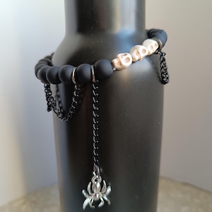 May include: Black beaded bracelet with white skull beads and dangling chains with a silver spider charm.