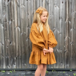 Girl wearing linen cinnamon color dress, loose fit, puffed sleeves, ruffle neck