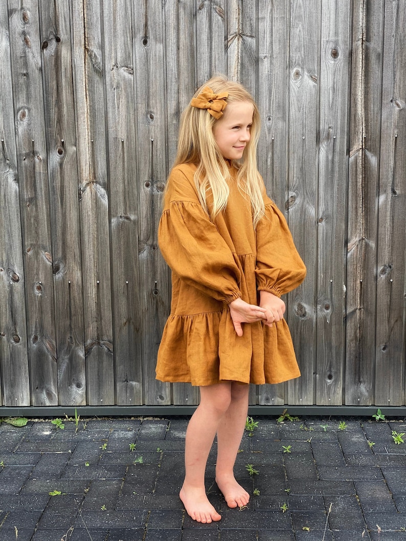 Girl wearing linen cinnamon color dress, loose fit, puffed sleeves, ruffle neck