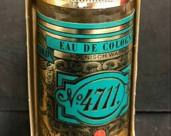 Puede incluir: Una botella de colonia azul y dorada con el texto "Eau de Cologne" y "No. 4711" en la etiqueta. La botella está en una caja azul y blanca con el texto "Spray" en la parte delantera.