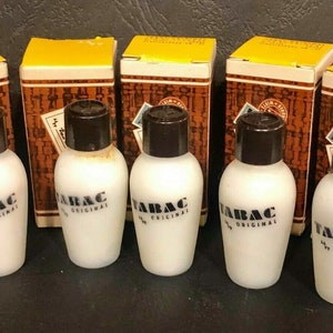 May include: Five small bottles of Tabac Original aftershave in white glass bottles with brown caps. The bottles are sitting on a brown surface in front of their original boxes, which are yellow and brown with a repeating pattern.