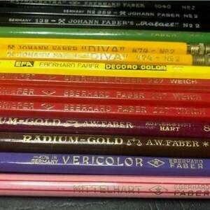 May include: A close-up of a stack of vintage coloured pencils. The pencils are all different colours and have different labels on them. The labels include the brand name "Eberhard Faber", the pencil grade, and the country of origin. The pencils are arranged in a stack, with the oldest pencils at the bottom and the newest pencils at the top.