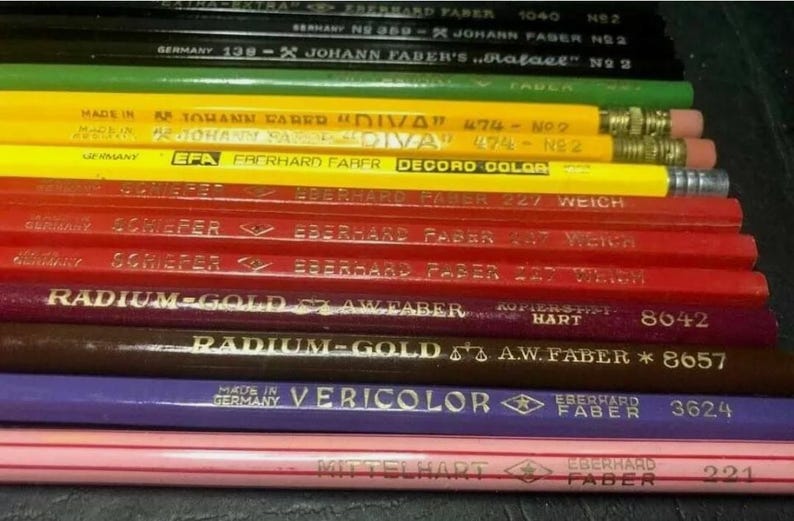 May include: A close-up of a stack of vintage coloured pencils. The pencils are all different colours and have different labels on them. The labels include the brand name "Eberhard Faber", the pencil grade, and the country of origin. The pencils are arranged in a stack, with the oldest pencils at the bottom and the newest pencils at the top.
