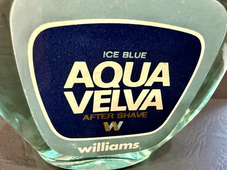 Puede incluir: Primer plano de un frasco de loci&oacute;n para despu&eacute;s del afeitado Aqua Velva. La etiqueta es azul oscuro con las palabras "ICE BLUE" y "AQUA VELVA" en blanco, y "AFTER SHAVE" en dorado. La marca "Williams" est&aacute; en la parte inferior.