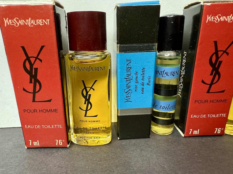 May include: Several Yves Saint Laurent miniature perfume bottles are displayed. The bottles are in red, black, and blue boxes. The bottles are labeled "Pour Homme" and "Eau de Toilette". The bottles are 7 ml.
