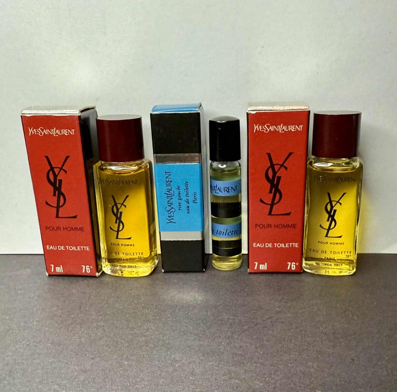 May include: An assortment of Yves Saint Laurent miniature perfume bottles and boxes. The bottles are filled with a yellow liquid and have dark brown caps. The boxes are red and black with the YSL logo and text.