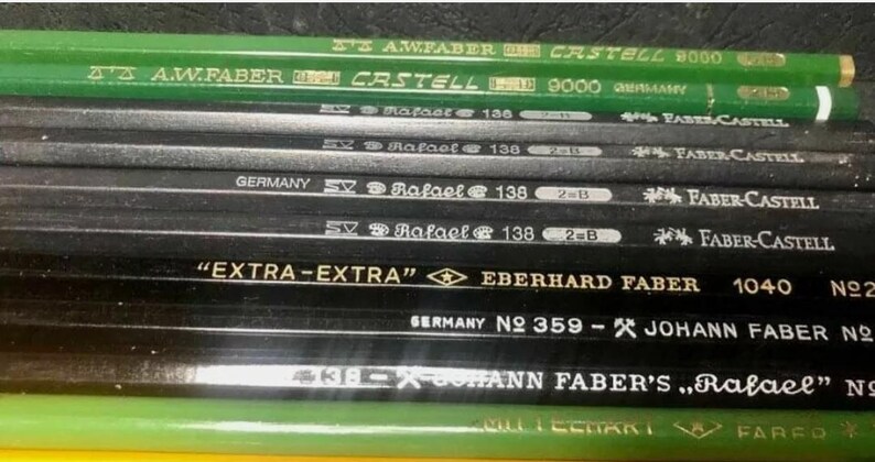 May include: Close-up of a collection of black and green pencils with various markings, including "EXTRA-EXTRA" Eberhard Faber 1040, "Germany No. 359 - Johann Faber No. 318", and "A.W. Faber Castell 9000 Germany".