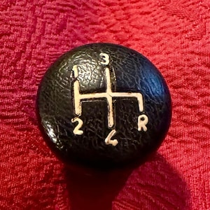 Op de afbeelding: Een zwarte leren versnellingspookknop met witte nummers 1, 2, 3, 4 en R.